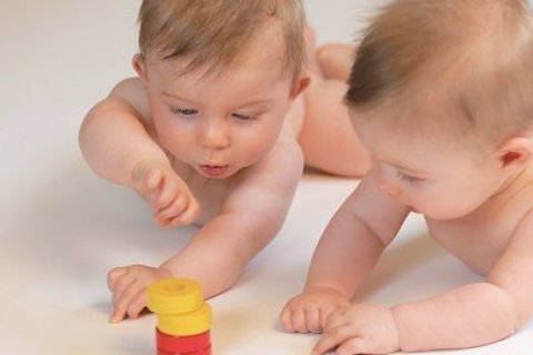 Zwei Babys erforschen in der PEKiP-Gruppe ein Spielzeug.