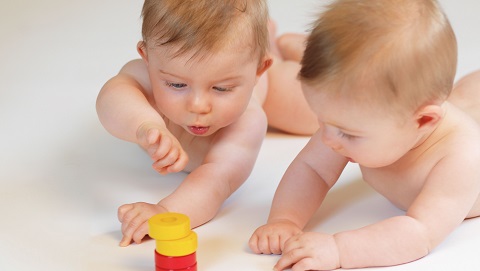 Zwei Babys untersuchen einen Turm aus gelben und roten Holzringen.
